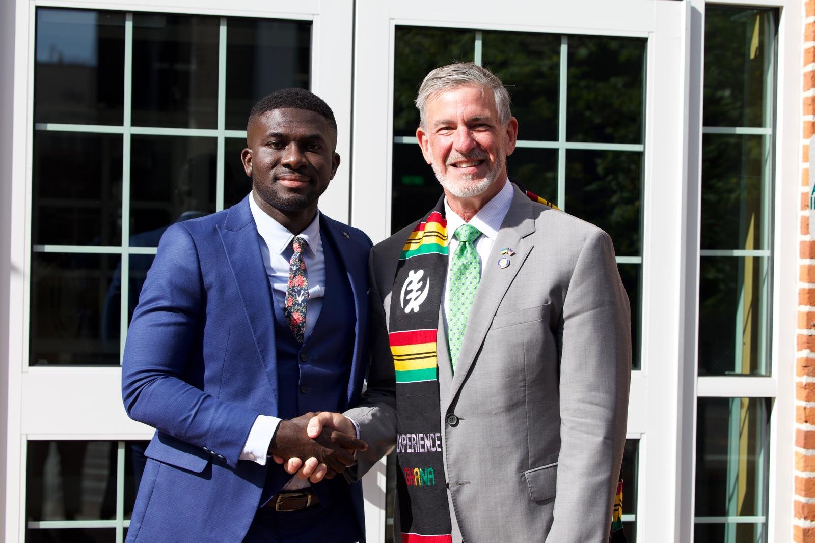 A member of the NSA delegation shaking hands with an Ohio University representative wearing a Ghanaian kente stole